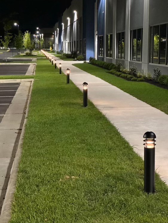 illuminated sidewalk at night next to grass and commercial building